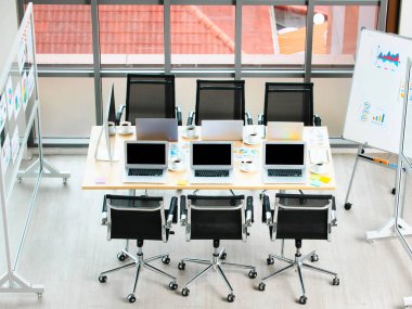 Bilgisayarlarla dolu boş şirket ofisindeki toplantı odası masasının en üst görüntüsü. Kahve fincanları veri raporları. Bina pencerelerinin yanındaki siyah sandalyeler ve cam tahtalar..