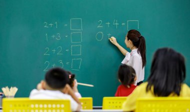 Asyalı güzel kadın matematik hocasının portre resmi elinde tebeşirle durup ilkokul matematik denklemi soruları yazarken bir grup erkek ve kız öğrencinin okuduğu karatahtaya.