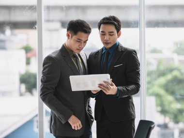 İki genç işadamı kağıda bakıyor. Planlarında beyin fırtınası yapıp gülümsüyorlar. Ofiste, meslektaşlarının açıklamaları iyi bir ortak olduğunu gösteriyor.