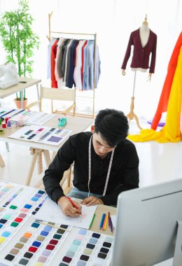 Profesyonel atölyede otururken Asyalı moda tasarımcısının renkli bir taslak oluşturması
