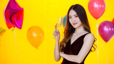 Asyalı, uzun saçlı seksi bir kızın, kırmızı kokteyl içkisini yudumlarken, uzun bardakta içki içerken, renkli balonların önünde, bulanık sarı arka planda partilerde,.