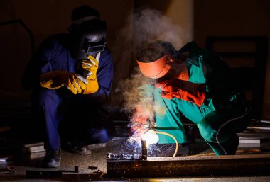 Tamirciler geceleri fabrikada fazla mesai yapmazlar. Tamirci tulumları, eldivenleri, botları ve metal kaynaklama kaskları olan güvenlik kıyafetleri giyen mühendisler..