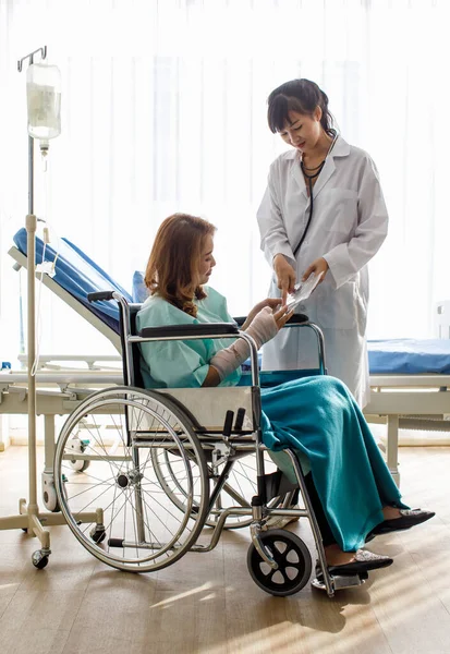 患者さんは車椅子に座って集中的に聴き入っていますが 医師が事故報告書では専門家のサポートで腕を骨折から回復する方法も説明しています — ストック写真