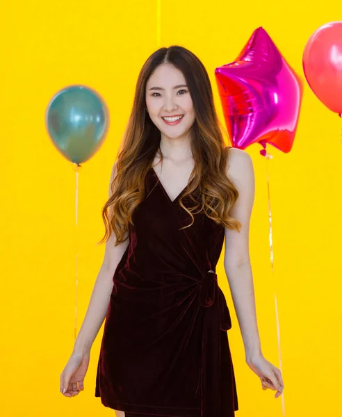亚洲年轻貌美的长发姑娘 穿着华丽的衣服 站在五颜六色的明星面前开心地笑着 黄色背景的圆形氦气气球在惊喜的晚会上 — 图库照片