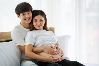 Sıcak aile kavramı. Erkek ve kadın Asyalı âşıklar hamile bir kadının karnına sevgi ve özenle dokunuyor. Karı ve kocanın ellerine odaklan.