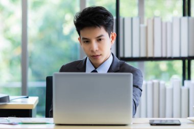 Şaşırmış Asyalı işadamı masaya oturup dizüstü bilgisayarla çalışırken eline yaslanıp projeyi düşünüyor.