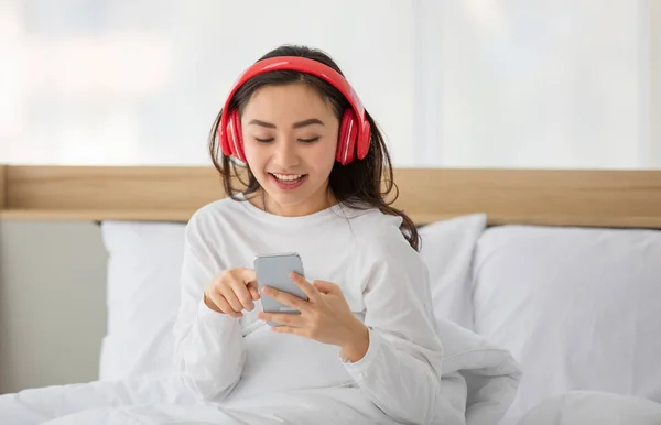 人気の音楽プレイリストを検索するためにデジタルスマートフォンを使用してカジュアルな白い服で若い大人のアジアの女性の肖像画のショット 十代の若者たちは 赤いヘッドフォンで音楽を聴くことを楽しむ — ストック写真