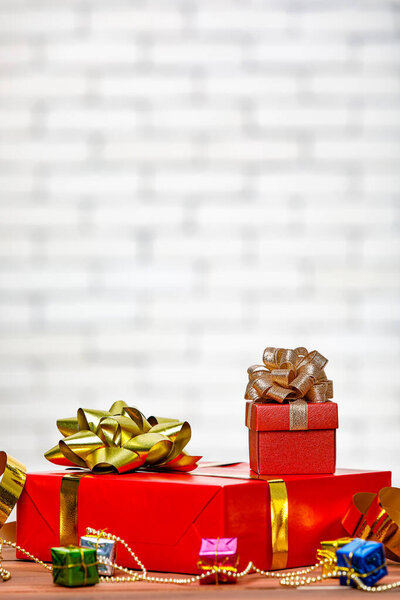 Studio shot of small and big red paper wrapped present gift boxes with gold and silver ribbon bow tie placed on wood table with decorative hanging sphere ball in front full decor Christmas pine tree.