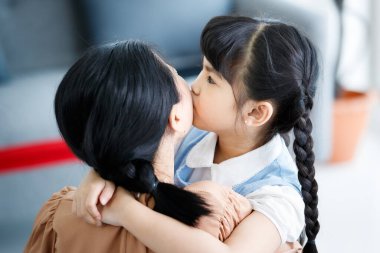 Asyalı, küçük, mutlu, anaokulu çocuğu kollarını boynuna dolayıp gülümseyen, sevgiyi kucaklayan genç ve sevimli anneyi yakından çek. Anne kucağında küçük bir çocuk taşıyor..