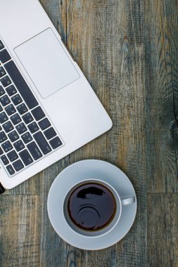 Dizüstü bilgisayarın üst görüntüsü, beyaz fincanda siyah kahve, ahşap desenli arka plan, kopyalama alanı olan..