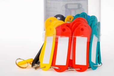 Üzerinde kırmızı sarı ve yeşil plastik isim etiketi olan metal halkalı anahtarlık, yukarıdan aşağıya, yuvarlak plastik silindir bir kutudan düşer. Beyaz arkaplanda izole.