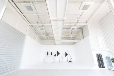 Beyaz duvarlara ve zemine ampuller ve klimalı profesyonel fotoğrafçı ekipmanları yerleştirilmiş geniş ve uzun, kapalı bir endüstriyel tasarım stüdyo atölyesi..