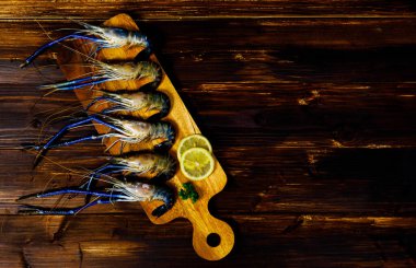 Yakın çekimde çiğ taze lezzetli lezzetli malzeme lezzetli büyük nehir kaplan karidesleri kesme tahtasında mavi pençeler ile süslenmiş siyah ahşap masa üzerinde boş metin alanı ile.