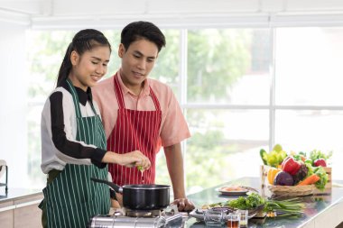 Asyalı, yakışıklı erkek arkadaş ve yakışıklı, yetenekli sevgili aşıklar mutfakta Tom Yam Kung pişirirken kadınlar baharatlı çorbaya limon suyu koyarken erkekler yakınlarda dururlar..