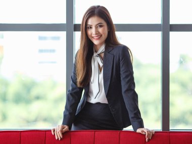 Neşeli Asyalı, Lao etnik kökenli iş kadını, iş merkezindeki koridordaki koltukta pozitif ve sıcak bir gülümsemeyle uzanan ve kameraya bakan.