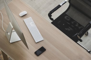 Masaüstü bilgisayarı, klavyesi, cep telefonu ve rahat ergonomik koltuğu olan, rahat bir ofis ya da işyeri olmayan modern ahşap masa. Yaratıcı tasarım, teknoloji kavramları