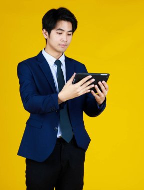 Not defterinde çalışan genç adam mavi takım elbise giyer. Sarı arka planlı stüdyo çekimi. Konsept iş, kariyer, bilgisayar, kopyalama alanı, odaklanma, yaşam tarzı