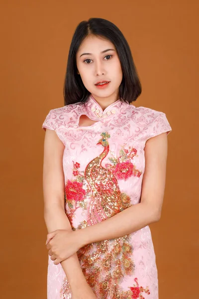 ポートレートクローズアップスタジオは ピンクの中国のCheongsam Qipao伝統的な孔雀 花のパターンドレスは茶色の背景に広告ポーズを持つカメラで見る — ストック写真