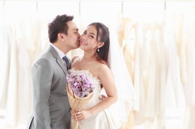 Damat ve gelin ayakta, gülümsüyor ve bir gelinin elbisesinin arkasında sarılıyorlar. Asyalı adam, tatlı yanaklı kadın aşkını temsil ediyor. En güzel düğün gününü kutlayalım.