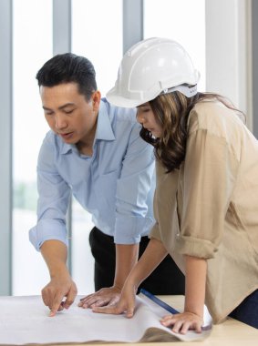 Asyalı mühendis ekibi, kadın ve erkek, bir bina projesi için ev planı hakkında konuşuyor ve tartışıyorlar..