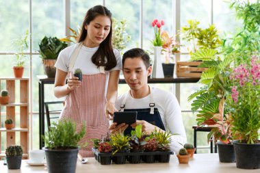 Modern erkek kadın bahçıvanlar sosyal medyada konuşan satış ağaçlarıyla yakınlaşırlar. İç dekorasyon için bitkilerle çevrili cam bir odada. Çevrimiçi alışveriş ve satış kavramı.