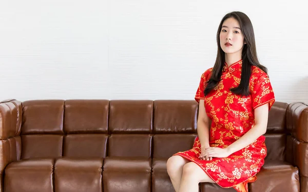 一位身穿红色传统服装 一头长长的黑发的中国美女 优雅地坐在棕色的沙发上 双手放在膝盖上 — 图库照片