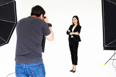 Asyalı genç, dost canlısı düz saçlı kadın model gülümsüyor ve kollarını kavuşturup poz veriyor ve fotoğrafçı stüdyoda çekim yapıyor..