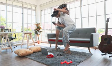 Genç ve çekici Asyalı çift ellerinde joysticklerle birlikte hoplayıp zıplamaktan ve video oyunları oynamaktan zevk alıyorlar. Oturma odasında cam pencereli eğlence ve heyecan dolu gözlükler takıyorlar..