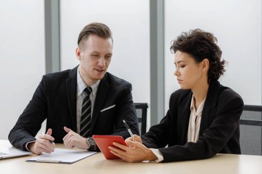 Zarif takım elbiseli neşeli erkek ve kadın girişimciler bilgisayar ve belgelerle masada oturmuş iş stratejilerini tartışıyorlar..