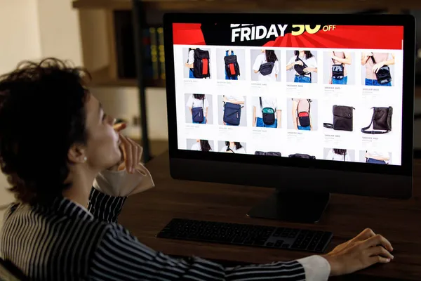 Kara Cuma günü alışveriş yaparken çevrimiçi mağazada çanta seçen kadın alıcıların arka planı% 50 satış ve bilgisayar monitörüne işaret ediyor