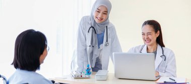 Müslüman Arap İslam tesettür ve beyaz laboratuvar önlüğü giyen Asyalı kadın doktor steteskop danışmanlığı yapıyor. Yatağın yanında tekerlekli sandalyedeki yaşlı kadın hastayla ve narmal salin solüsyonla ilgili sorular soruyorlar..