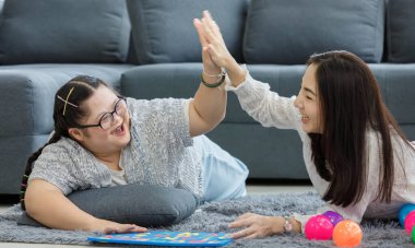 Asyalı bir anne ve Down sendromlu bir kız sayısal blok oyunu oynuyorlar ve el ile beşlik çakıyorlar..