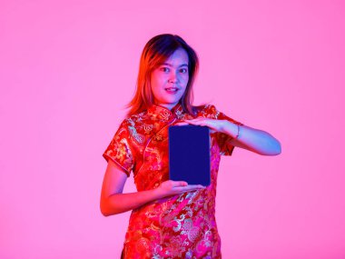 Asya kökenli genç bir kızın portre çekimi. Güzel, geleneksel Çin geleneksel Cheongsam Qipao tişörtü giymiş. Elinde pembe ışık arka planında boş monitör dokunmatik tableti var..