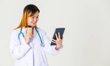 Asya 'nın başarılı, kendine güvenen, laboratuvar önlüklü, steteskop takan kadın doktorunun stüdyo fotoğrafı. Beyaz arka planda elinde tablet bilgisayarla gülümseyerek kahve molası veriyor..