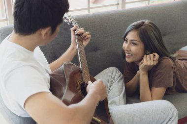 Genç ve çekici Asyalı çift kanepede birlikte. Oturan adam gitar çalıyor ve kadın cam zeminli oturma odasında yalan söylüyor ve dinliyor. Aşk ve çift ilişkisi kavramı.