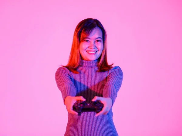 ポートレートクローズアップスタジオショットのアジアの若いですティーン女性モデルゲーマーでグレーTurtleeckドレス立って笑顔開催3DビデオゲームDualshackコンソールジョイスティックで手遊びでピンクの光と背景 — ストック写真