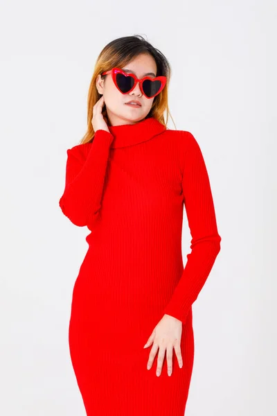 アジアの自信に満ちた女性ファッションモデルのポートレートスタジオショットカジュアルなファッショナブルな流行の赤の長袖タートルネックドレスでハート形の黒レンズサングラススタンドセクシーポージング上の白の背景 — ストック写真