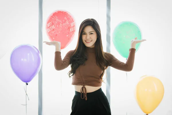 身着棕色长袖上衣的亚洲年轻快乐女性站在彩色气球前微笑的肖像工作室照片模糊了背景 — 图库照片