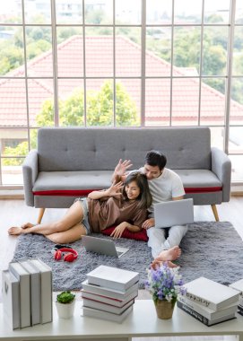 Genç Asyalı çift rahat tişörtler giyip evde dizüstü bilgisayarla çalışıyorlar. Evden çalışma kavramı.