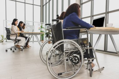 Tekerlekli sandalyede oturan engelli kadın da dahil Asyalı iş kadınları ofiste dizüstü bilgisayarla sıkı çalışıyorlar. İş görüşmesi için kavram.