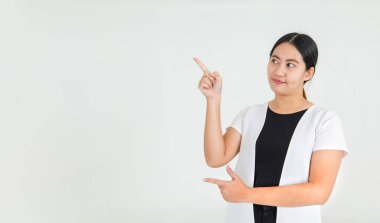 Sevimli Asyalı kız mutlu bir şekilde gülümsüyor ve ilginç bir yön ve inanılmaz bir mesaj vermek için parmağıyla işaret ediyor. Güzel kız çekici bir eğitim ve uyarı sunmaktan memnuniyet duyar..