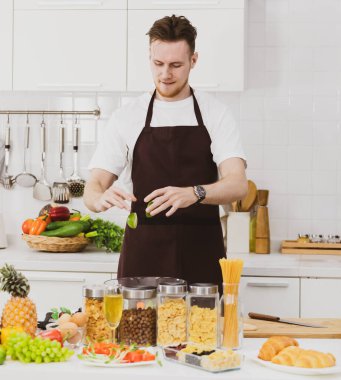 Anonim erkek aşçı, modern mutfaktaki çeşitli ürünlerle yemek pişirirken tahtanın üzerine olgun kireç döker.