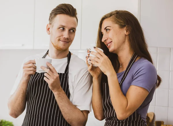 Casal Encantado Aventais Bebendo Bebidas Quentes Balcão Com Utensílios Cozinha — Fotografia de Stock