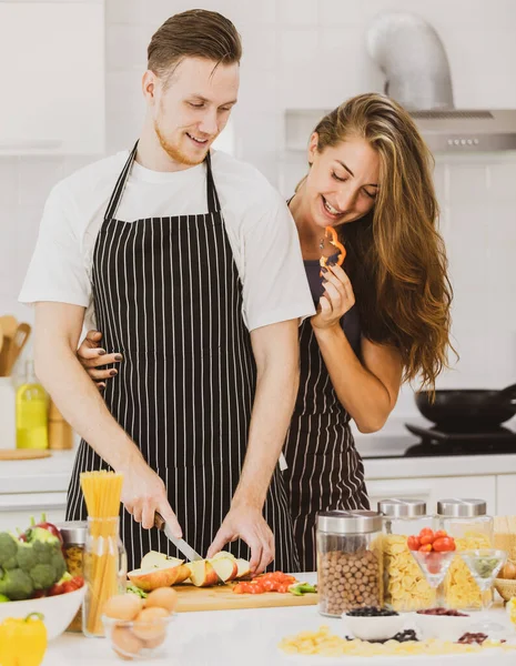 Sevgilisinin yanında duran olumlu kız arkadaş evdeki hafif mutfakta çeşitli ürünlerle masada elma kesiyor.