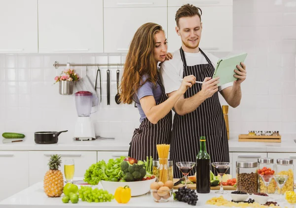 Casal Conteúdo Aventais Surfar Tablet Enquanto Está Mesa Com Produtos — Fotografia de Stock