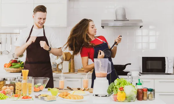 Casal Otimista Aventais Dançando Mesa Com Ingredientes Variados Liquidificador Enquanto — Fotografia de Stock