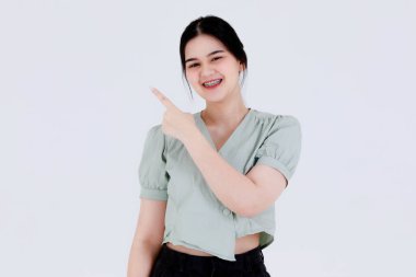 Asyalı genç kadın modelin günlük kıyafet giymiş, ayakta poz veren, reklam yapan ve beyaz arka plandaki boş alana el uzatan portresi..