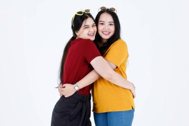 Portre stüdyosu, iki güzel Asyalı, şık moda bayan arkadaş resmi çekti. Günlük kıyafetler ve moda gözlükleri takmış, gülümseyen, gülümseyen, beyaz arka planda sarılan kameralara bakıyordu..