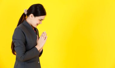 Asyalı profesyonel, başarılı, kendine güvenen, resmi üniformalı hostes ve eşarplı, gülen eşarplı, sarı arka plandaki yolcuya saygılarını sunan kadın hostesin stüdyo fotoğrafı..