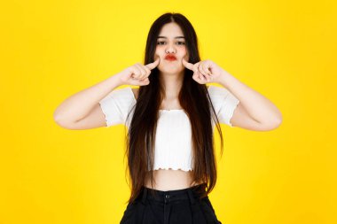 Asyalı, genç, güzel, uzun siyah saçlı kadın modelin portre çekimi. Kırpılmış üst kıyafet giymiş ve sarı arka planda neşeli bir şekilde poz veriyor..